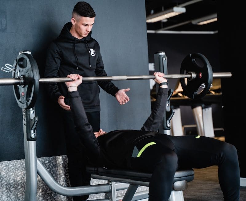 personal trainer with client doing bench press