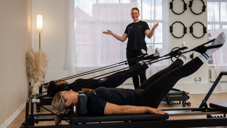 Pilates instructor teaching students how to use a reformer.