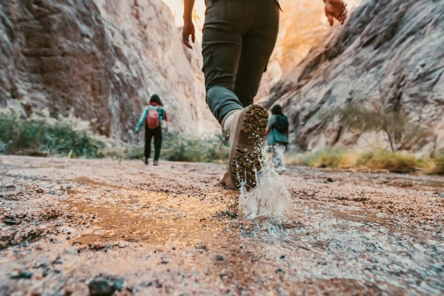 A man hikes in a canyon, wading through shallow water