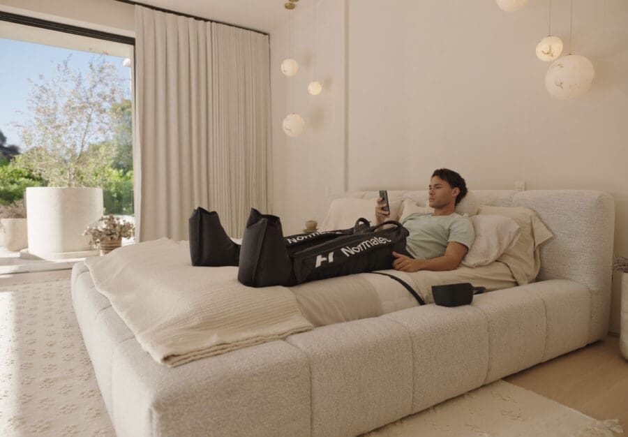 Client using Hyperice Normatec recovery boots after assisted stretching exercises to support circulation and muscle recovery.